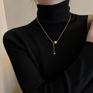 Elegant gold spherical pendant necklace with snake chain on black knitwear background