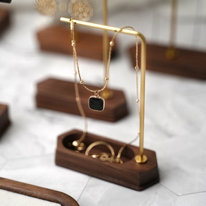 Golden necklace with black square pendant on a solid wood base metal jewelry stand