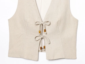Détail de gilet en lin avec fermeture à nouer et perles en bois marron en beige