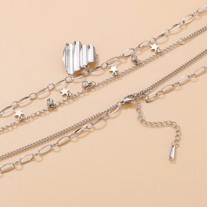 Détail d'un collier argenté à plusieurs couches avec pendentifs étoiles et médaillon ondulé