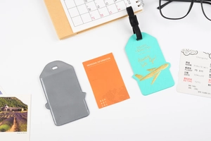 Flat lay of turquoise travel luggage tag with gold airplane and orange information card
