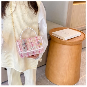 Close-up of pink plaid crossbody bag with pearl handle and cute rabbit doll on a child