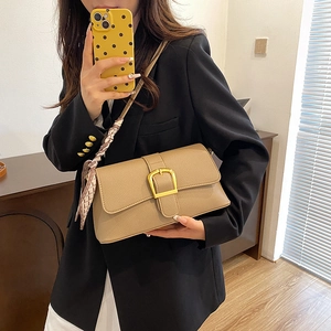 Khaki leather shoulder bag with gold buckle and patterned silk scarf held by a model