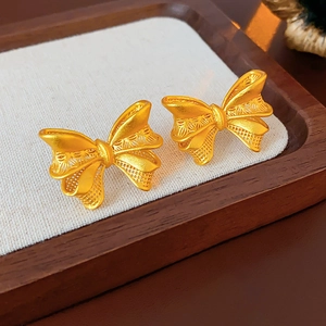 Detailed macro view of 18K gold bow-shaped earrings with hollow mesh texture on linen