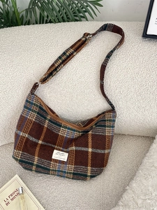 Brown vintage plaid dumpling bag in wool fabric with adjustable strap on a cozy sofa