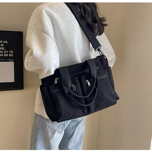 Detail of black corduroy shoulder bag showing multi-pocket design and strap texture