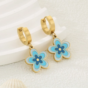 Détail de boucles d'oreilles créoles dorées avec fleurs en émail bleu sur décor blanc
