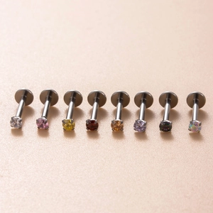 Titanium labret studs set with various colored zircon gemstones on beige background