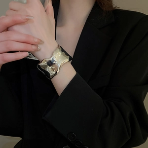 Macro view of chunky irregular golden cuff bracelet with a polished wavy mirror finish