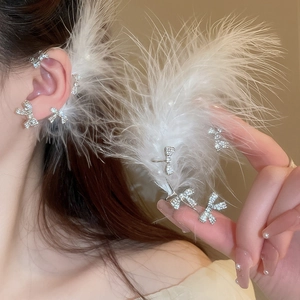 Detailed close-up of bow-knot ear cuff with sparkling rhinestones and white feathers