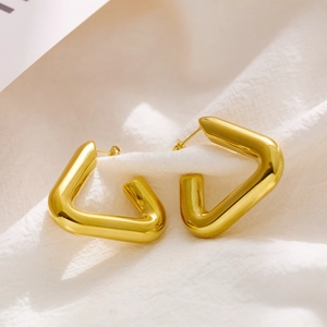 Detailed view of polished gold geometric hoop earrings on soft white fabric background