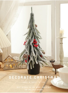 Mini snow-flocked Christmas tree with red berries and pine cones on a wooden desk