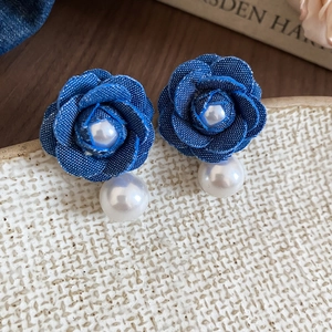 Macro detail of handmade denim rose earrings with large white pearls and floral texture
