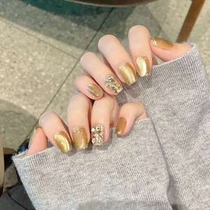 Unghie finte dorate Maillard cat-eye con strass 3D su mani della modella