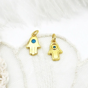 Detail of 18K gold plated Hamsa Hand charms with blue enamel eye on white lace