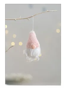 Pink plush Christmas gnome ornament hanging on a branch with warm festive bokeh lighting