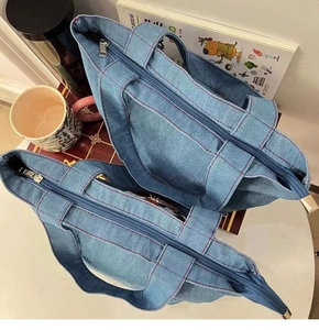 Detailed view of blue denim tote bag with red stitching, metal zipper, and sturdy handles