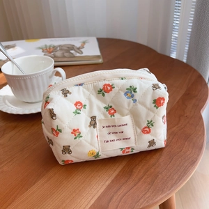 Quilted makeup bag with cute bear and red floral pattern on a warm wooden table