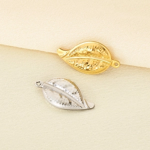 Macro shot of minimalist gold and silver leaf charms on textured beige fabric background