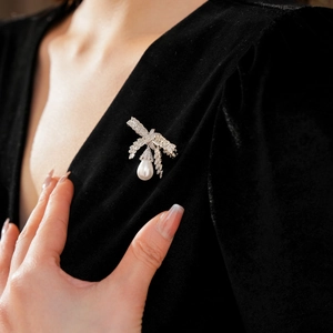 Détail macro d'une broche nœud argentée sertie de zircons avec perle goutte blanche