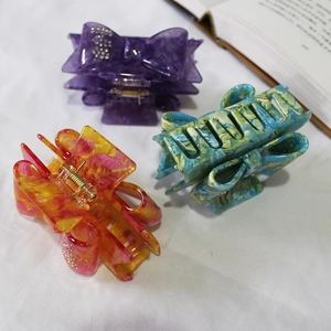 French bow hair claws set with rhinestones in purple, orange and teal on white fabric