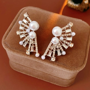 Macro detail of fan-shaped gold earrings with white pearls and sparkling rhinestones