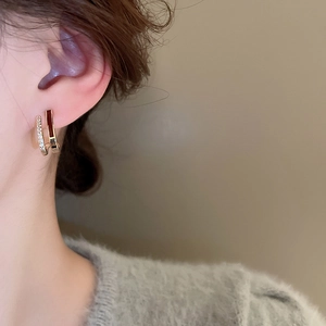 Close-up of elegant gold double-hoop earrings with zircon and red enamel on model