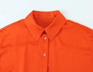 Close-up of orange satin shirt collar with silky texture and matching buttons