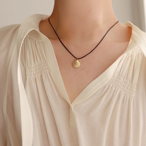 Detailed close-up of a golden scallop shell pendant on a thin black cord necklace