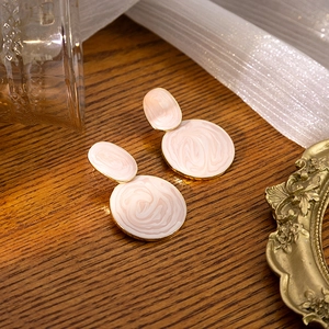 Detail of pink marble textured resin earrings on a vintage wood and tulle background