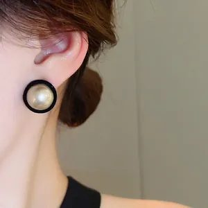 Minimalist round faux pearl stud earrings with black flocking frame worn by a model