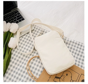 Close-up of a white canvas crossbody bag with adjustable beige strap on plaid background