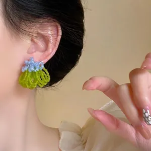 Detail shot of light blue and green beaded tassel earrings worn by a model in a natural setting