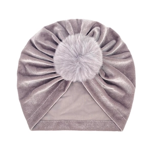 Plush mauve velvet baby turban hat with a large faux fur pompom on a white background
