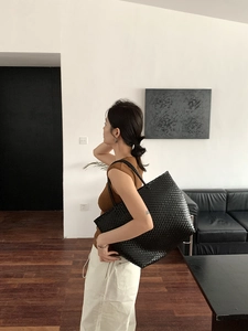 Modern black woven tote bag shown on model for size perspective in minimalist setting