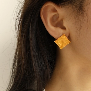 Minimalist square gold stud earrings with textured woven pattern on female model ear