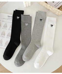 Flat lay of ribbed knee-high socks in black, grey, and white with bow embroidery details