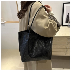 Detail of a large black tote bag with snakeskin texture worn by a model in a beige coat