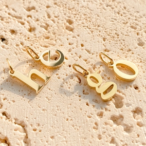 Close-up of polished gold alphabet charms h, e, g, o with oval loops on stone texture