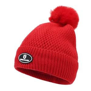 Detail of red winter knit hat featuring a fluffy pom-pom and a Teddy Island bear patch