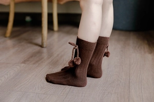 Detailed view of dark brown ribbed knit baby socks with soft pom-pom drawstring detail