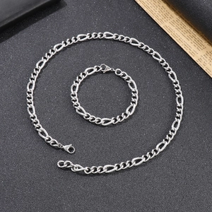 Flat lay of a silver Figaro chain necklace and bracelet set on a textured black backdrop
