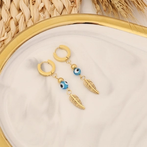 Detailed shot of gold evil eye and feather pendant earrings on a marble tray