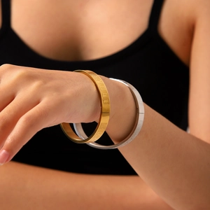 Detail of gold and silver Roman numeral steel bangles worn on the wrist for a chic look