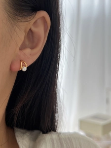 Close-up of elegant gold curved pearl earrings worn on a model's earlobe