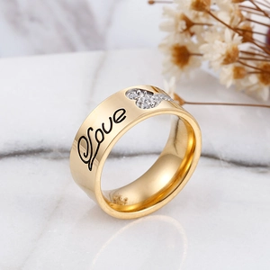 Gold wide band ring with Love engraving and heart-shaped zircon on marble surface