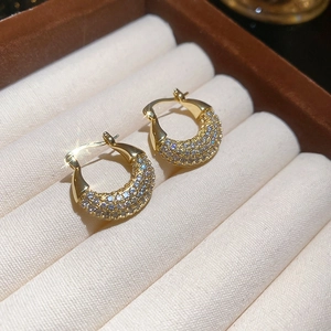 Detail of gold zircon hoop earrings displayed on a soft beige velvet jewelry box surface