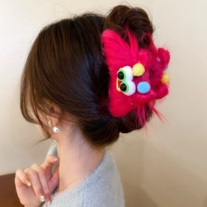 Pink plush monster hair claw clip with colorful pom-poms on a model's braided bun hairstyle