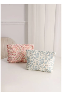 Detail of floral makeup bag set in pink and blue fabric with brand label on white desk