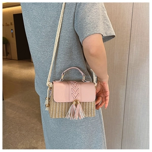 Pink patchwork straw crossbody bag featuring decorative tassels and braided rope strap